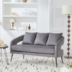 Modern velvet loveseat settee with cross back design, three decorative pillows, and metal legs in a living room setting