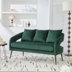 Modern velvet loveseat settee with cross back design, three decorative pillows, and metal legs in a living room setting