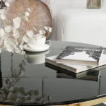Modern circular coffee table with stainless steel base and tempered glass top on wooden floor