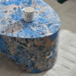 Goldoma oval blue fiberglass coffee table with marble-like finish in a modern living room