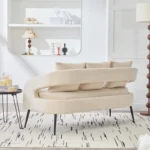 Modern velvet loveseat settee with cross back design, three decorative pillows, and metal legs in a living room setting
