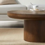 Modern round coffee table with wood veneer top and cylindrical legs in a living room setting