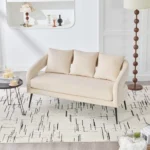 Modern velvet loveseat settee with cross back design, three decorative pillows, and metal legs in a living room setting
