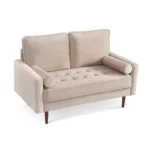 Goldoma 57-inch beige velvet loveseat with tufted seat, track arms, dark brown wood legs, and two toss pillows in a modern living room