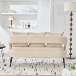 Modern velvet loveseat settee with cross back design, three decorative pillows, and metal legs in a living room setting