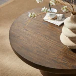 Modern round coffee table with wood veneer top and cylindrical legs in a living room setting
