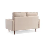 Goldoma 57-inch beige velvet loveseat with tufted seat, track arms, dark brown wood legs, and two toss pillows in a modern living room