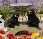 The outdoor bear figurine set against a backdrop of green shrubs and colorful flowers in a sunny garden.