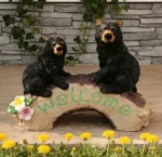 The bear family statue placed near a garden gate, with a 'Welcome' sign attached to the mother bear's front.