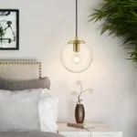 Three-quarter view of brass hanging light against a white wall, glass ball reflecting light.