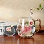 Elegant crystal glass tea mug with enamel floral design and handgrip on a wooden table