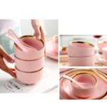 Elegant dinnerware set with gilt rim pink porcelain plates, bowls, mugs, and cutlery on a table
