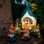 White gnome statue with solar light on roof, placed on grass near garden flowers at dusk.