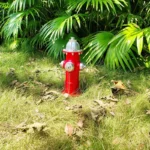 Wide shot of fire hydrant statue in a garden, surrounded by shrubs.