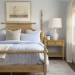 Natural wood nightstand with one drawer and a shelf beside a bed in a bedroom