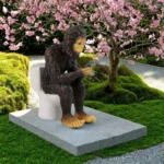 The sasquatch statue in a flower bed, surrounded by colorful blooms and mulch, emphasizing its outdoor decor role.