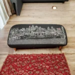 Goldoma 38-inch black wool ottoman with brown legs and nailhead trim used as a stylish footrest in a modern living room