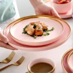 Elegant dinnerware set with gilt rim pink porcelain plates, bowls, mugs, and cutlery on a table