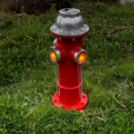 Red resin fire hydrant statue with gold paw print, placed on green grass in a sunny garden setting.