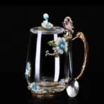 Elegant crystal glass tea mug with enamel floral design and handgrip on a wooden table