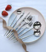 Elegant stainless steel flatware set with forks, spoons, and knives arranged on a wooden table