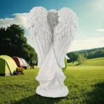 Close-up of white resin angel figurine with gold wings, holding a lantern, in outdoor setting.