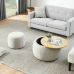 Goldoma round storage ottoman in beige fabric with hinged lid, used as end table with a cup on top, in a living room setting
