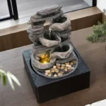 Close-up of the top tier of the Goldoma LED fountain showing water flowing over textured stone-like surface, soft blue