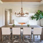 Rustic chandelier with distressed bronze finish, displayed in a living room with exposed beams and a stone fireplace.