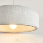 Close-up of the textured matte black metal shade and natural linen cord of the hanging light fixture against a white