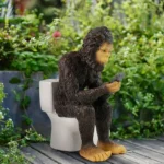 Angle shot of the sasquatch on the toilet, with a garden hose and birdbath in the background, showcasing its whimsical