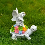 Front view of the resin angel riding turtle solar light, set against a wooden fence with potted plants.