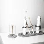 Gray toothbrush holder with a built-in toothpaste dispenser next to a bathroom sink.