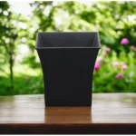 Side view of black square pot planter on a balcony railing, with city skyline in soft focus