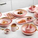 Elegant dinnerware set with gilt rim pink porcelain plates, bowls, mugs, and cutlery on a table