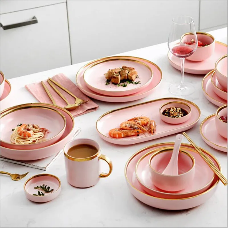 Elegant dinnerware set with gilt rim pink porcelain plates, bowls, mugs, and cutlery on a table