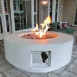 30-inch round propane fire pit table in grey color on a patio with cushions