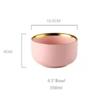 Elegant dinnerware set with gilt rim pink porcelain plates, bowls, mugs, and cutlery on a table