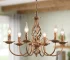 Rustic farmhouse chandelier with six lights in bronze iron, hanging over a wooden dining table with chairs in a cozy