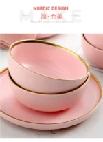 Elegant dinnerware set with gilt rim pink porcelain plates, bowls, mugs, and cutlery on a table