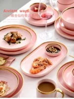 Elegant dinnerware set with gilt rim pink porcelain plates, bowls, mugs, and cutlery on a table