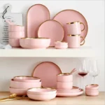 Elegant dinnerware set with gilt rim pink porcelain plates, bowls, mugs, and cutlery on a table