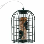 Side view of the green bird feeder hanging on a shepherd's hook in a sunny backyard garden.