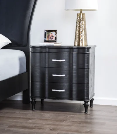 Black solid wood nightstand with curved front and turned legs in a bedroom setting