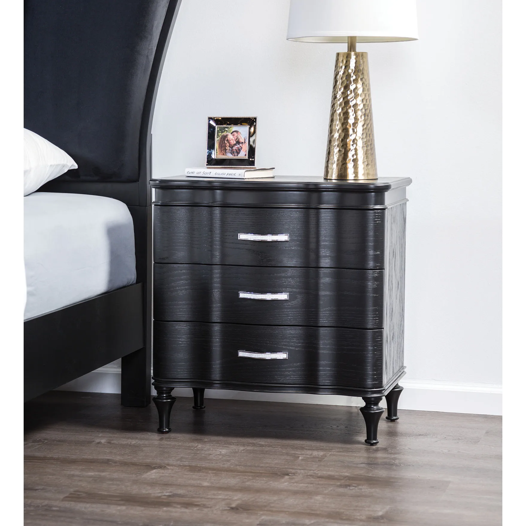 H72695bf221424846bc1bee0f1866ac10y.webp Black solid wood nightstand with curved front and turned legs in a bedroom setting