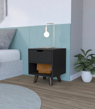 Modern nightstand with drawer and open shelf in black finish with wooden legs on a bedroom floor next to a bed