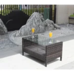 Outdoor coffee table with clear tempered glass top and brown PE rattan frame on a patio