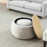 Goldoma round storage ottoman in beige fabric with hinged lid, used as end table with a cup on top, in a living room setting