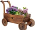 Wooden wagon planter box with four wheels, filled with flowers, on a patio.