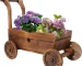 Wooden wagon planter box with four wheels, filled with flowers, on a patio.
